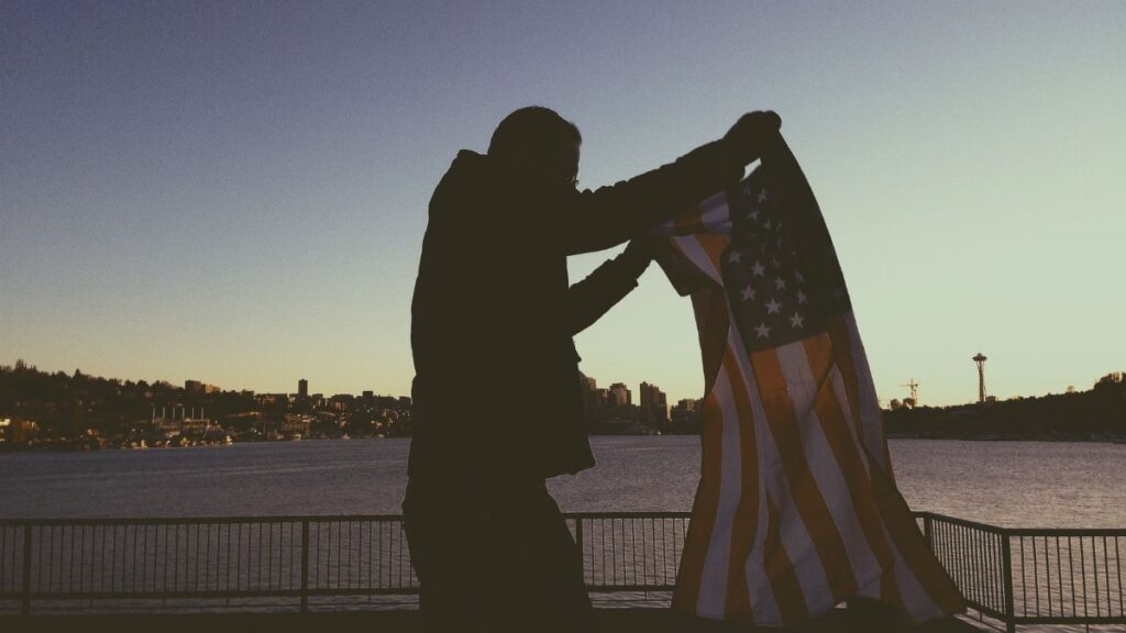 Person holding an American flag with Seattle skyline in the background at sunset.