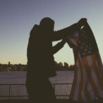 Person holding an American flag with Seattle skyline in the background at sunset.