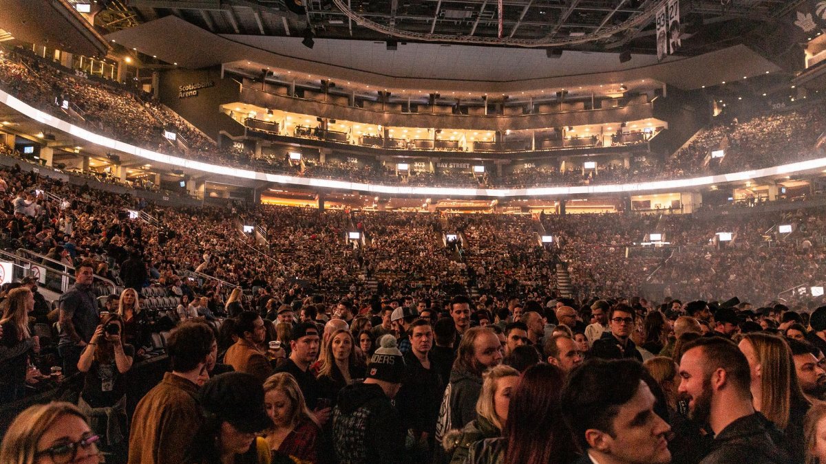 A large crowd gathers in an indoor arena for a lively event, surrounded by bright lights.