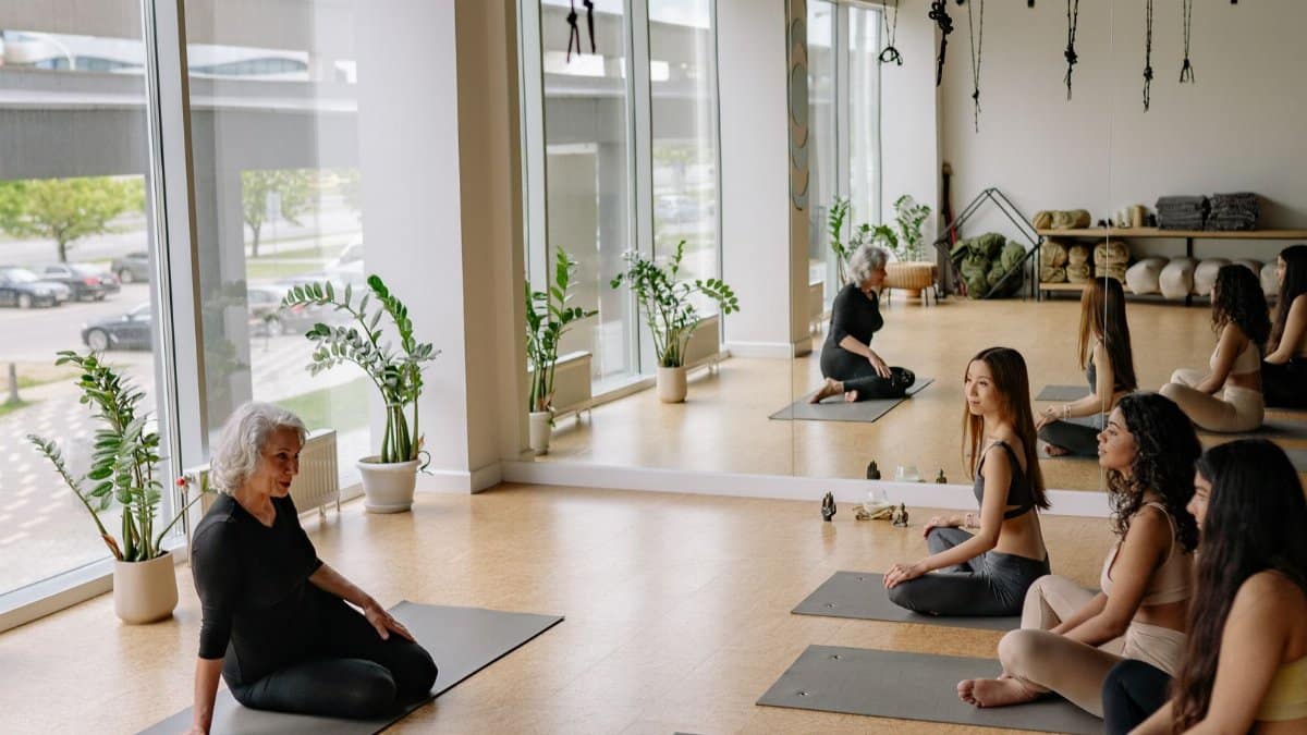 Yoga class with diverse women practicing in a bright, plant-filled studio with mirrors.