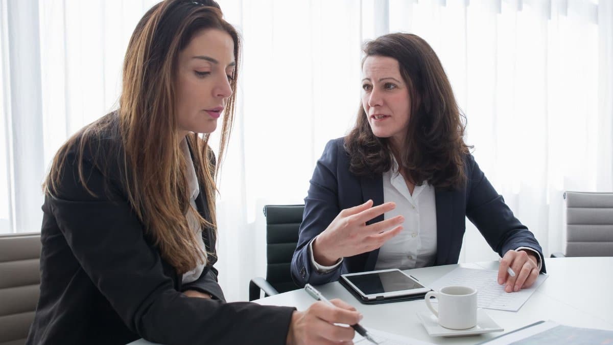 Two women in a business meeting discussing ideas while taking notes.