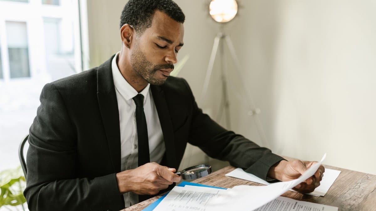 Professional man examines paperwork with magnifying glass at office desk, highlighting attention to detail.