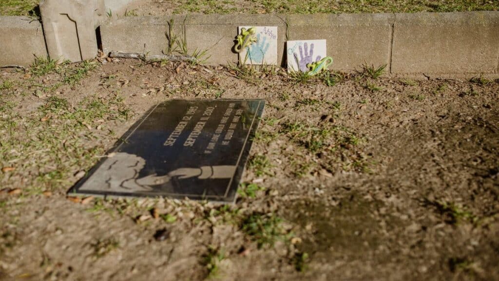 A gravesite with a memorial plaque and children's art in a cemetery setting.