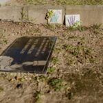 A gravesite with a memorial plaque and children's art in a cemetery setting.