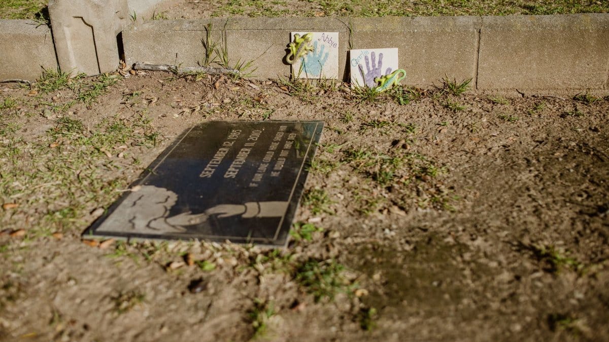 A gravesite with a memorial plaque and children's art in a cemetery setting.