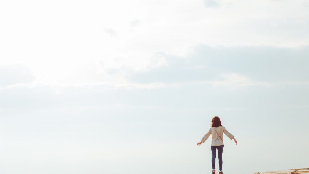 A woman standing on a hilltop embracing the open sky with a sense of freedom.