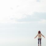 A woman standing on a hilltop embracing the open sky with a sense of freedom.