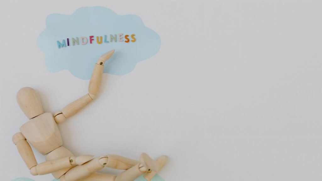 Wooden mannequin with mindfulness text on light blue cloud background, conveying calm.