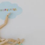 Wooden mannequin with mindfulness text on light blue cloud background, conveying calm.