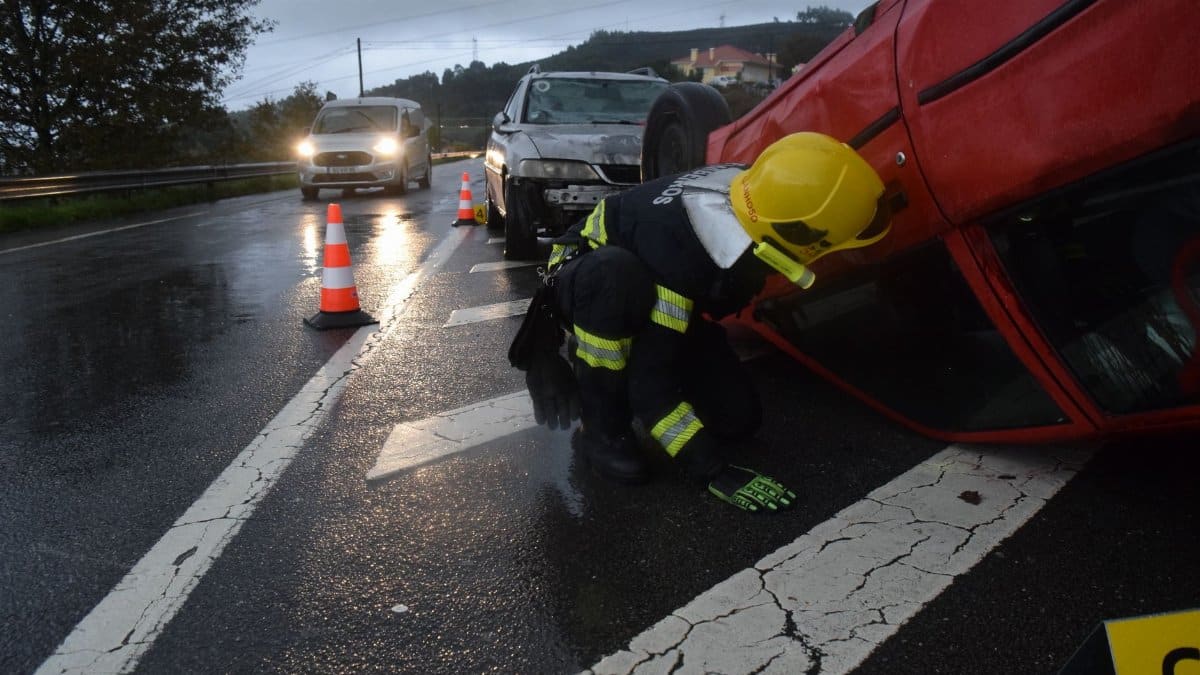 Firefighter attending to an overturned car on a rainy road in Póvoa de Lanhoso, Braga, Portugal.