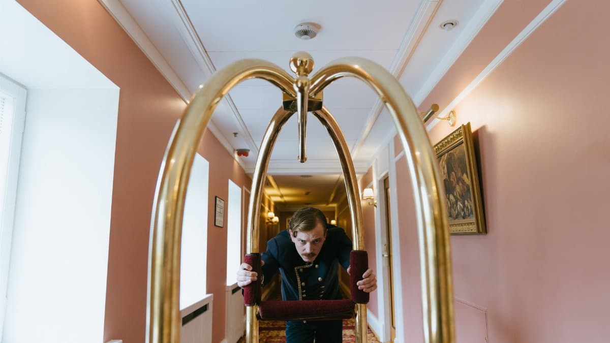 A bellboy pushes a luggage cart down a luxurious hotel corridor, embodying service and elegance.
