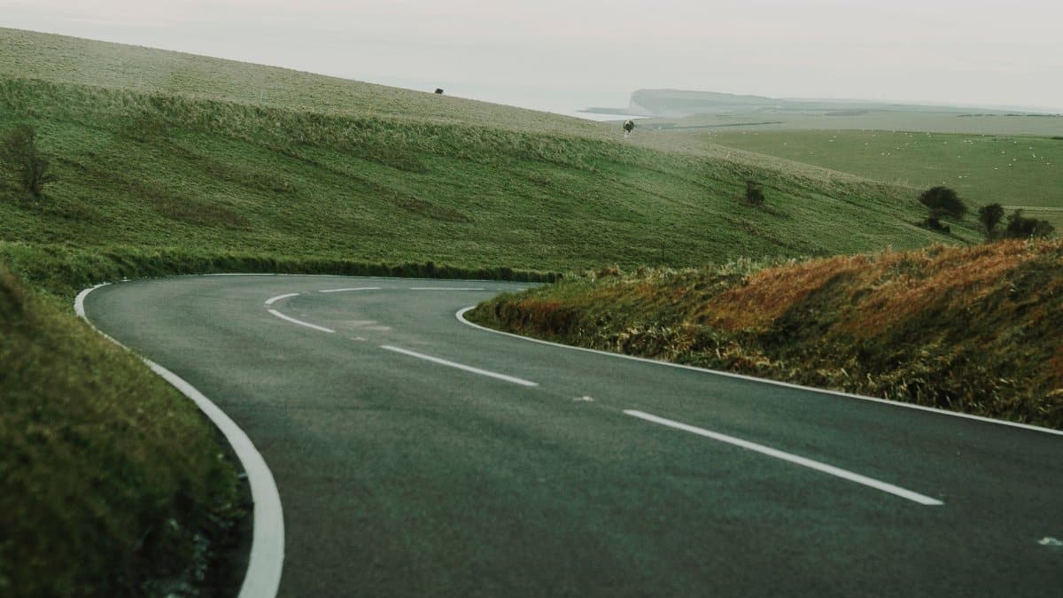 A serene curved road winding through lush green hills with distant views, ideal for travel themes.