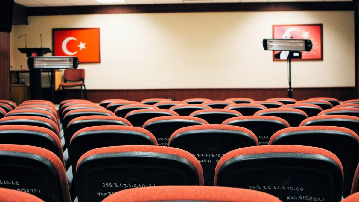 An empty conference room featuring red seats, a stage, and Turkish flags, ready for a meeting or presentation.