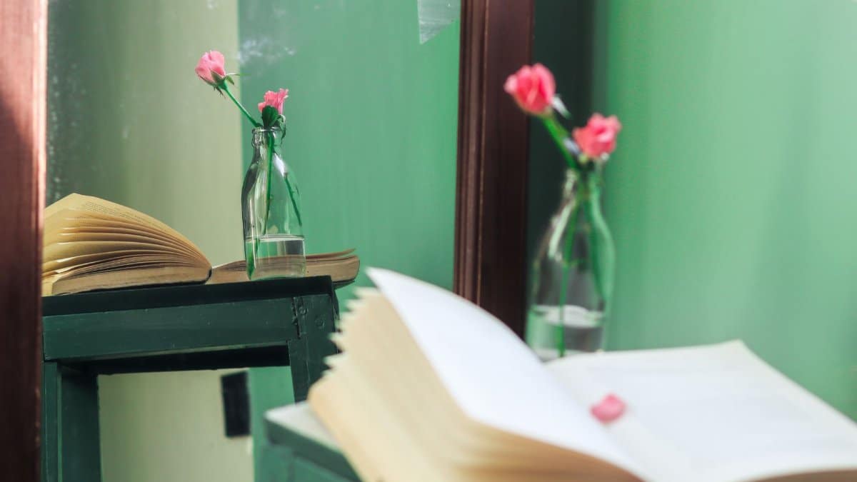 A peaceful reading area with open books and pink flowers reflecting in a mirror.