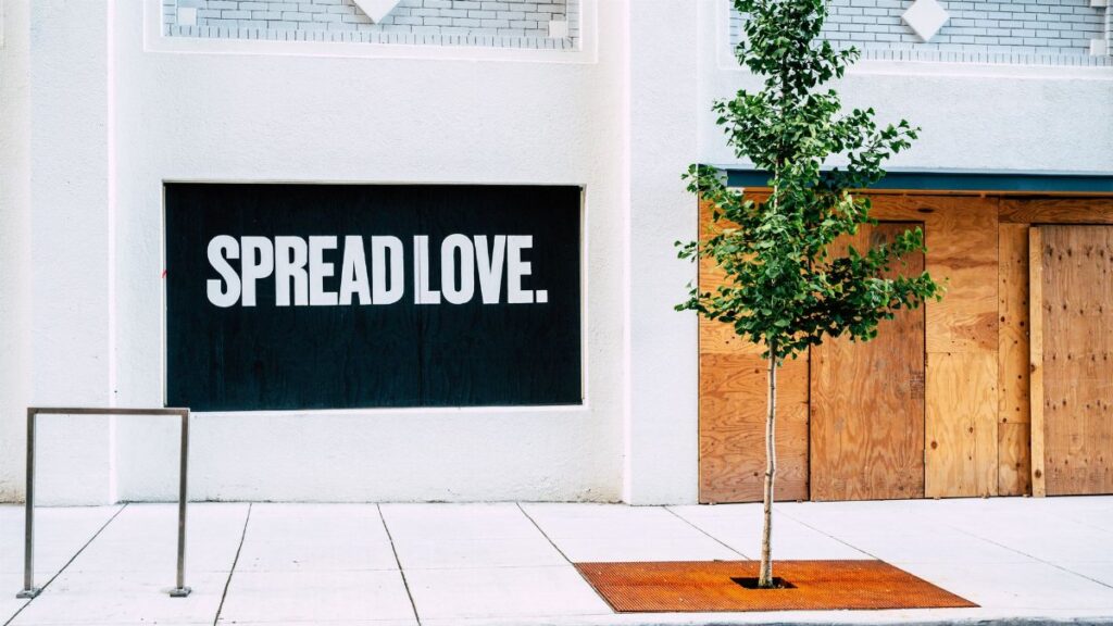 Street view with 'Spread Love' mural and a young tree on a sidewalk.