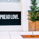 Street view with 'Spread Love' mural and a young tree on a sidewalk.