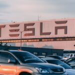 Tesla factory with parked cars during sunset, showcasing modern automotive industry vibes.