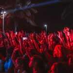 A lively crowd enjoying a night outdoor music festival under bright stage lights.