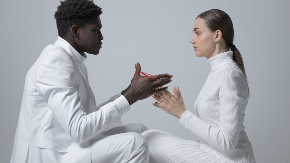 Two people in white outfits engage in conversation indoors; minimalism theme.