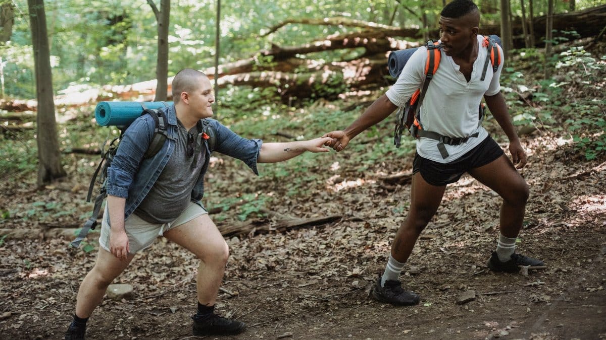 Full body of African American male hiker supporting boyfriend while walking through green woods