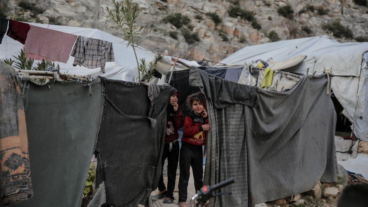 Two children stand outside a makeshift shelter in a Syrian refugee camp, capturing resilience in adversity.