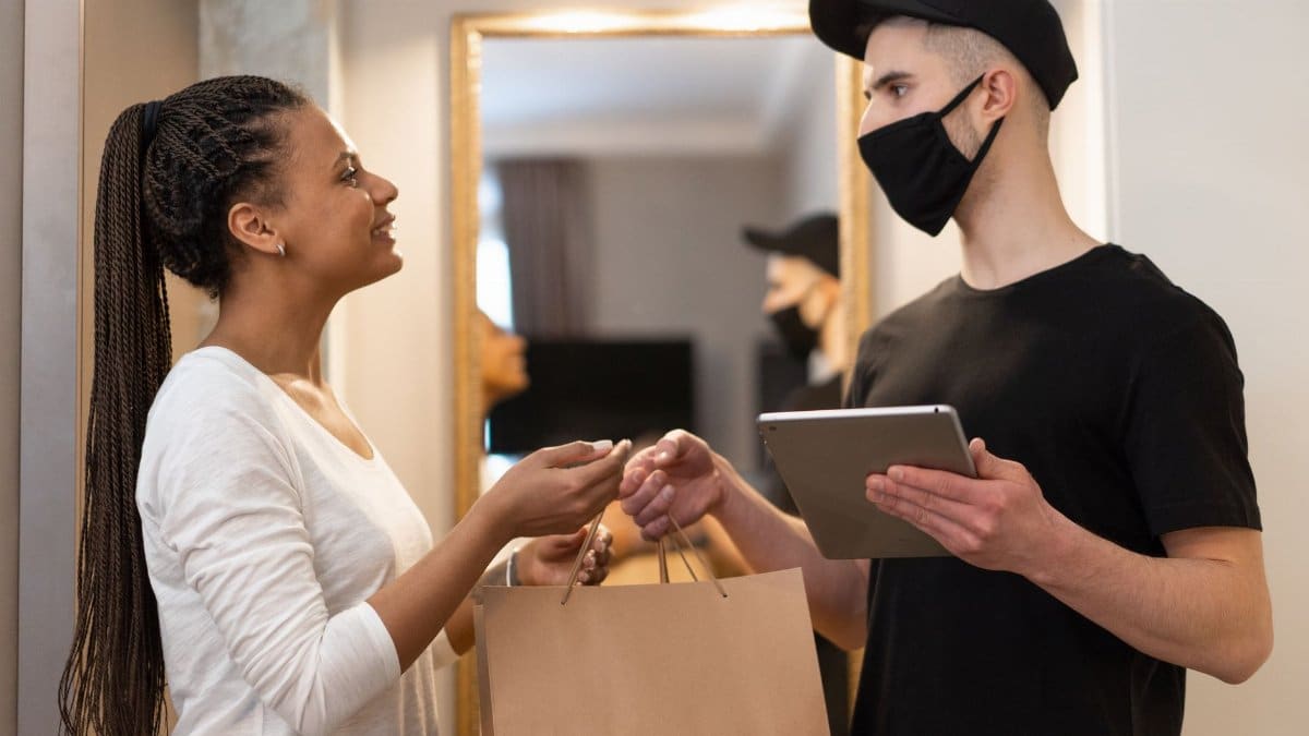 Woman receives package from masked delivery man at home, ensuring safe and efficient service.