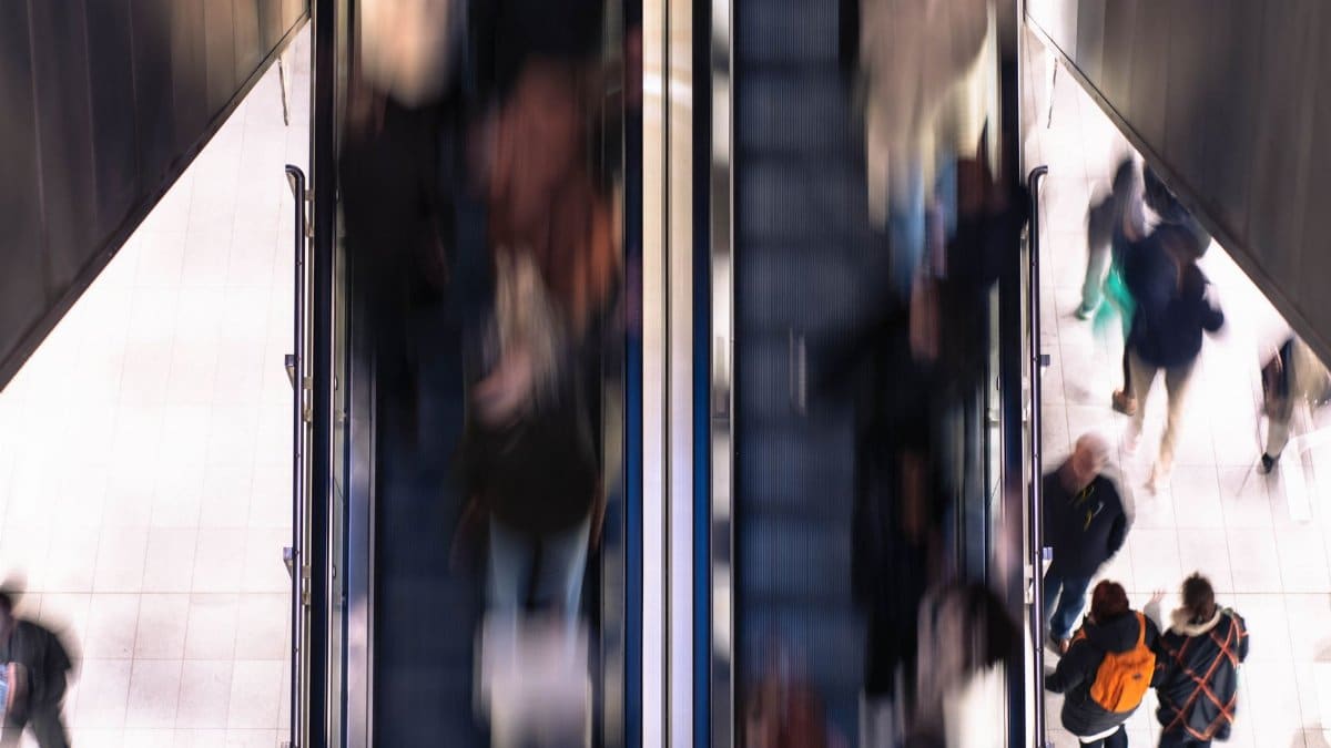 Blurred motion of people on escalators indoors, capturing urban hustle and movement.