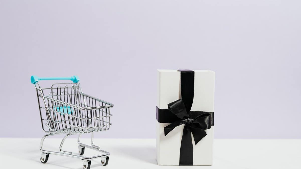 Minimalist shopping concept with cart and gift box tied with black ribbon.