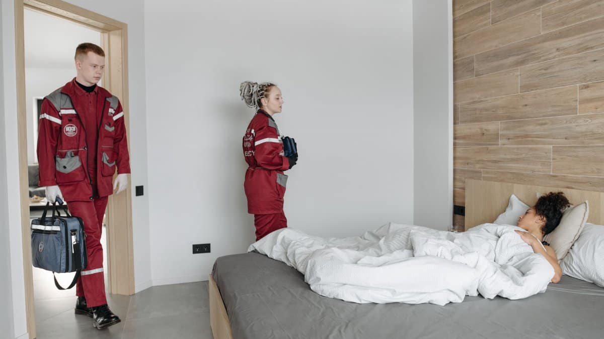 Paramedics assisting an unwell woman lying in bed, showcasing medical intervention indoors.