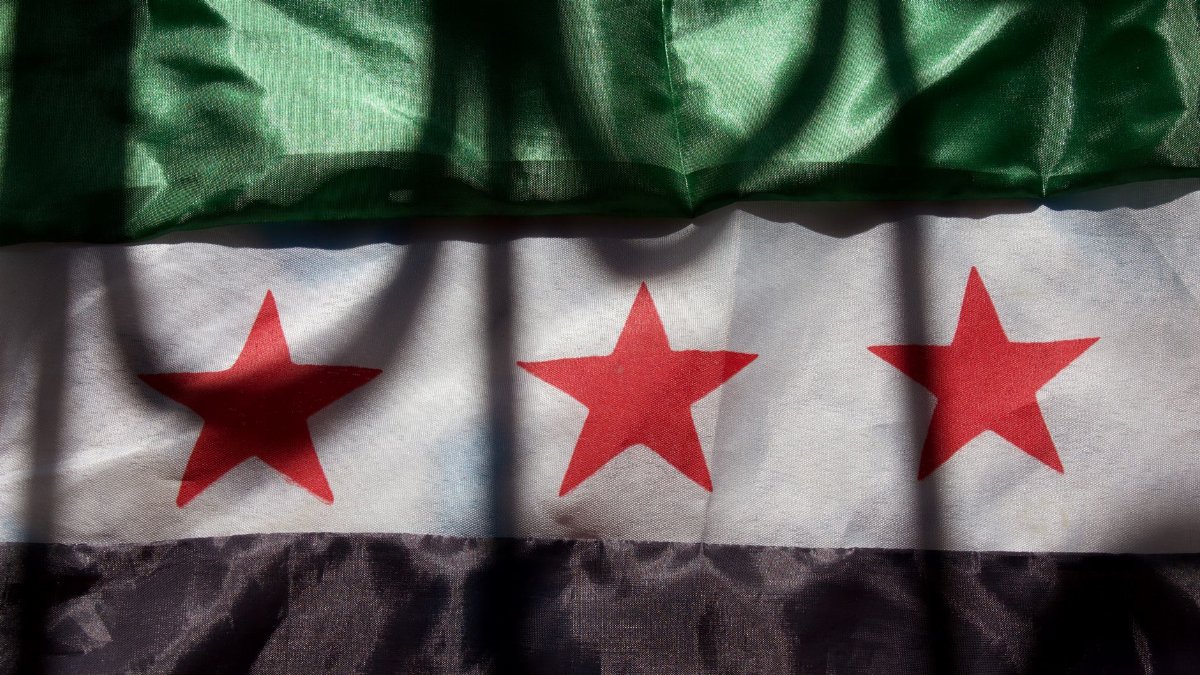 A close-up of the Syrian flag showing green, white, and black stripes with red stars.