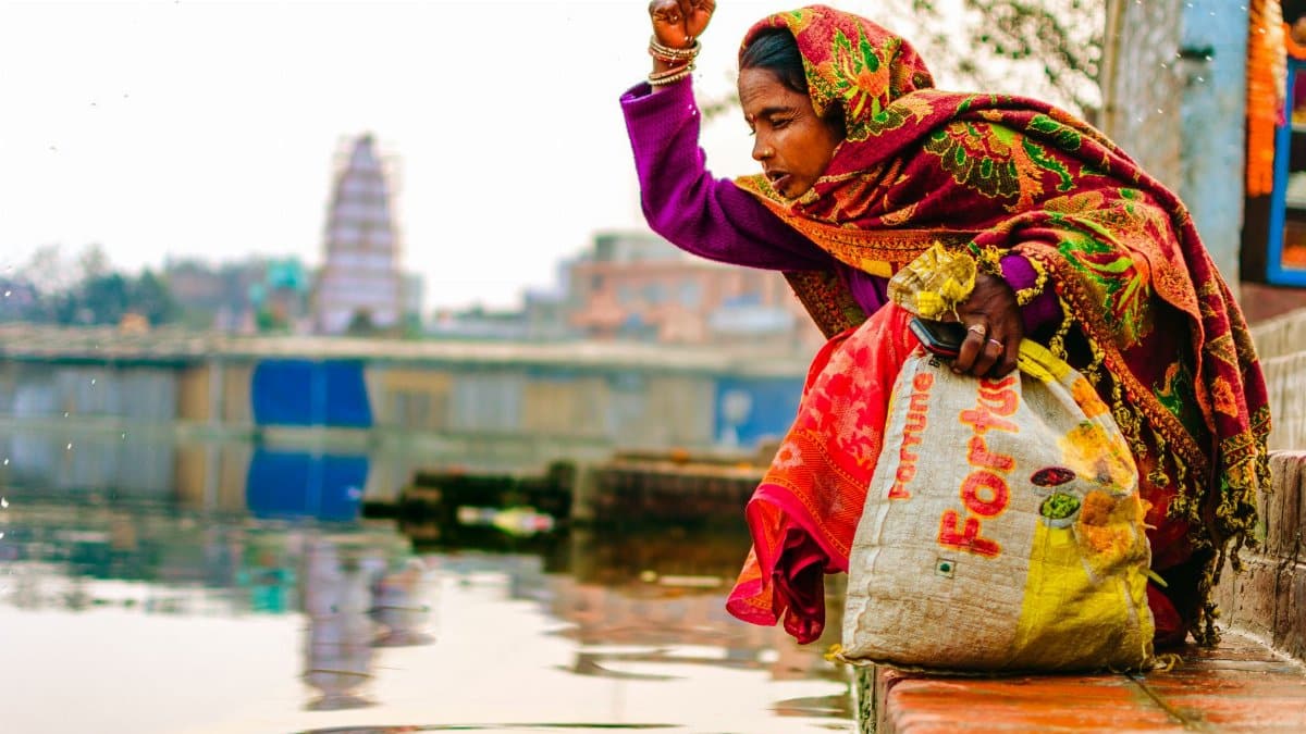 A woman performs a traditional ritual by a river in India, displaying cultural and religious practices.