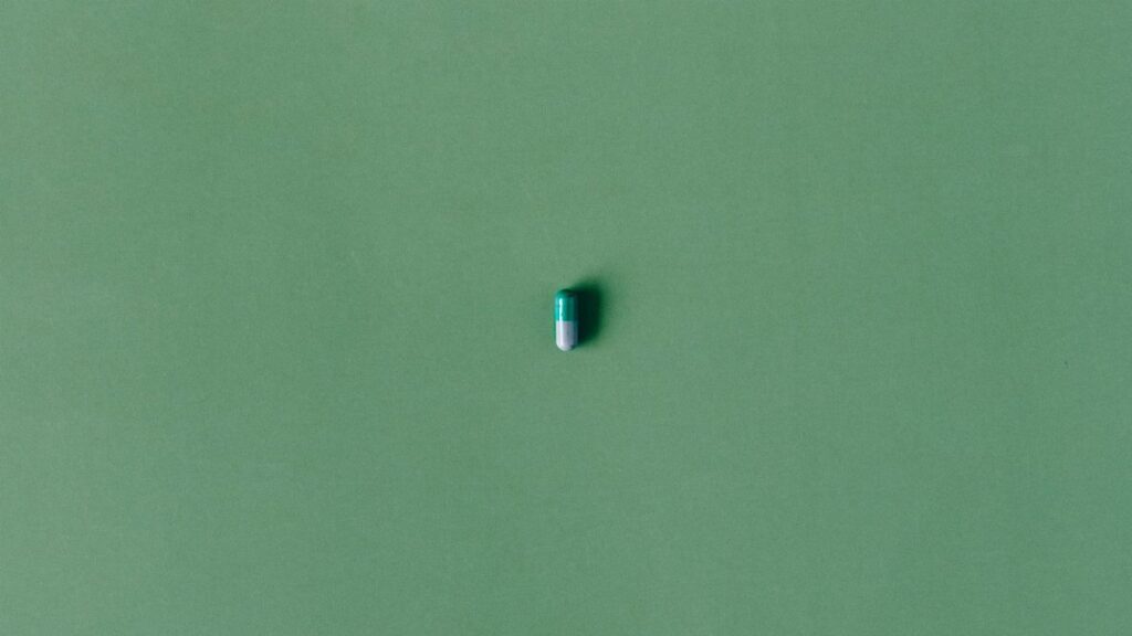 A single green capsule pill isolated against a matching solid green background.