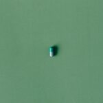 A single green capsule pill isolated against a matching solid green background.