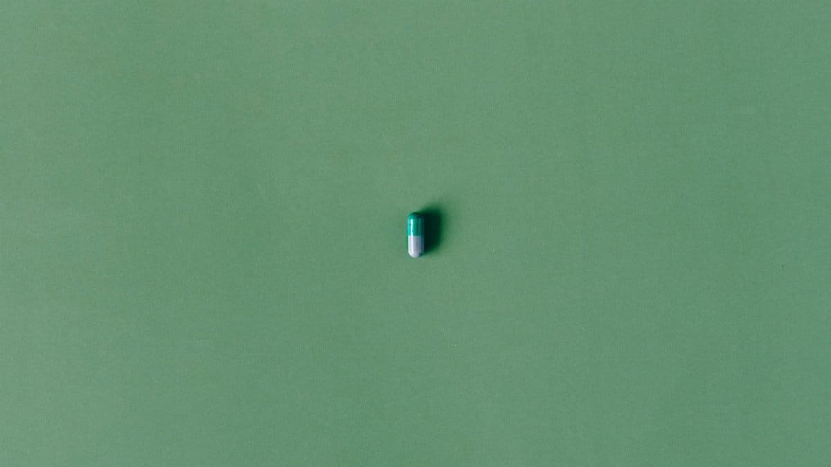 A single green capsule pill isolated against a matching solid green background.
