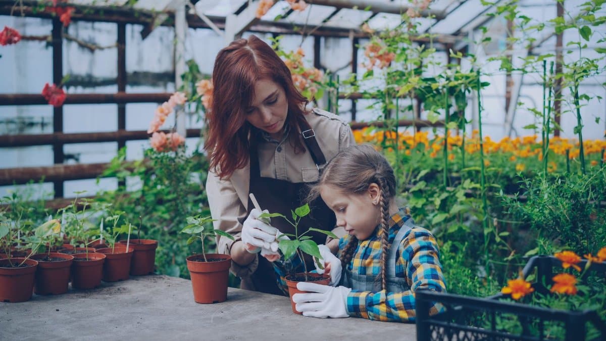 A woman and child gardening together in a vibrant greenhouse setting.