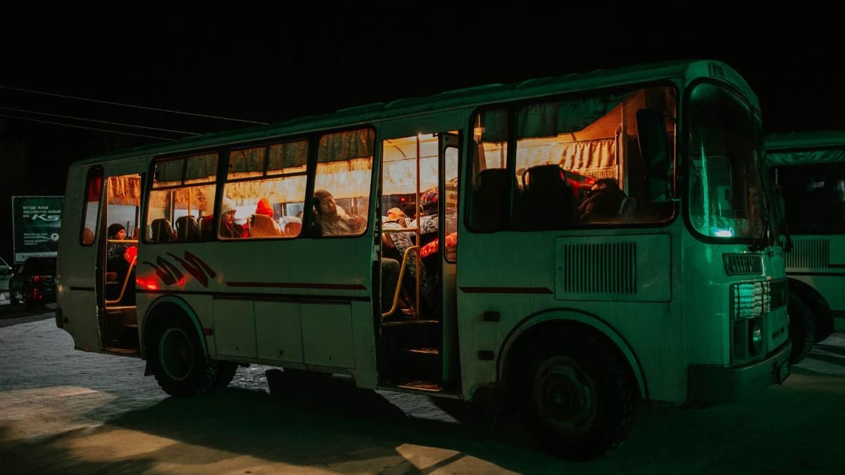 A bus parked at night with passengers visible inside, creating a warm, inviting glow.