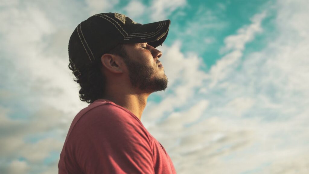 A man enjoys outdoor relaxation and mindfulness beneath a bright, cloudy sky, exuding calm and peace.