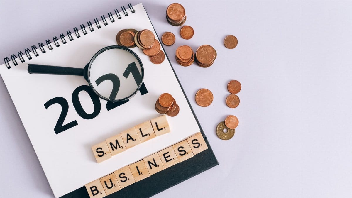 Flat lay of 2021 calendar, coins, magnifying glass, and 'small business' scrabble tiles.