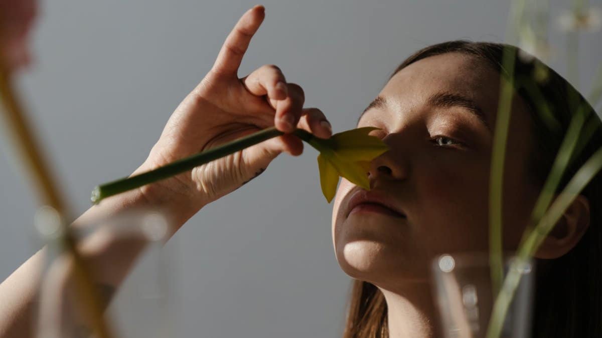 Adult woman gently smelling a daffodil flower indoors, captured in warm natural light.