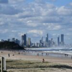 Picturesque view of Gold Coast beach with city skyline under a vibrant sky, capturing surf and sand.