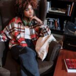A woman with curly hair in an armchair enjoying music with a vintage vinyl setup.