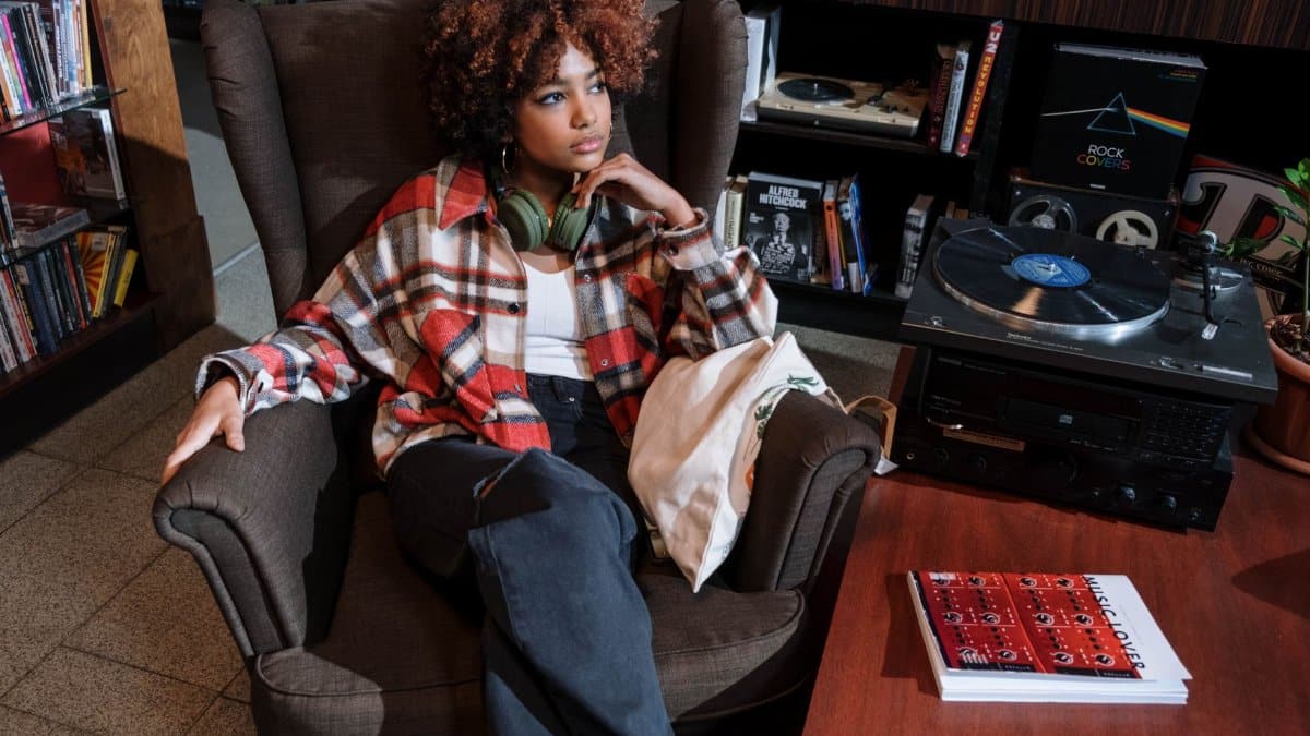 A woman with curly hair in an armchair enjoying music with a vintage vinyl setup.