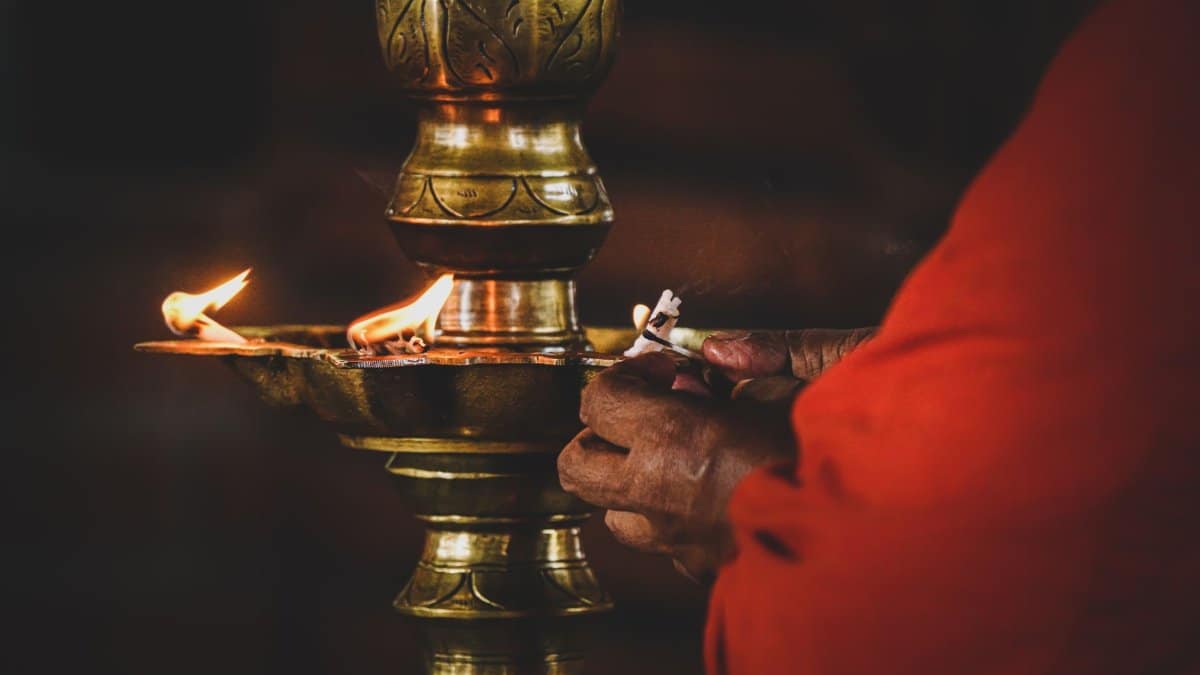 A person in red lighting an oil lamp during a religious ceremony, symbolizing devotion and tradition.