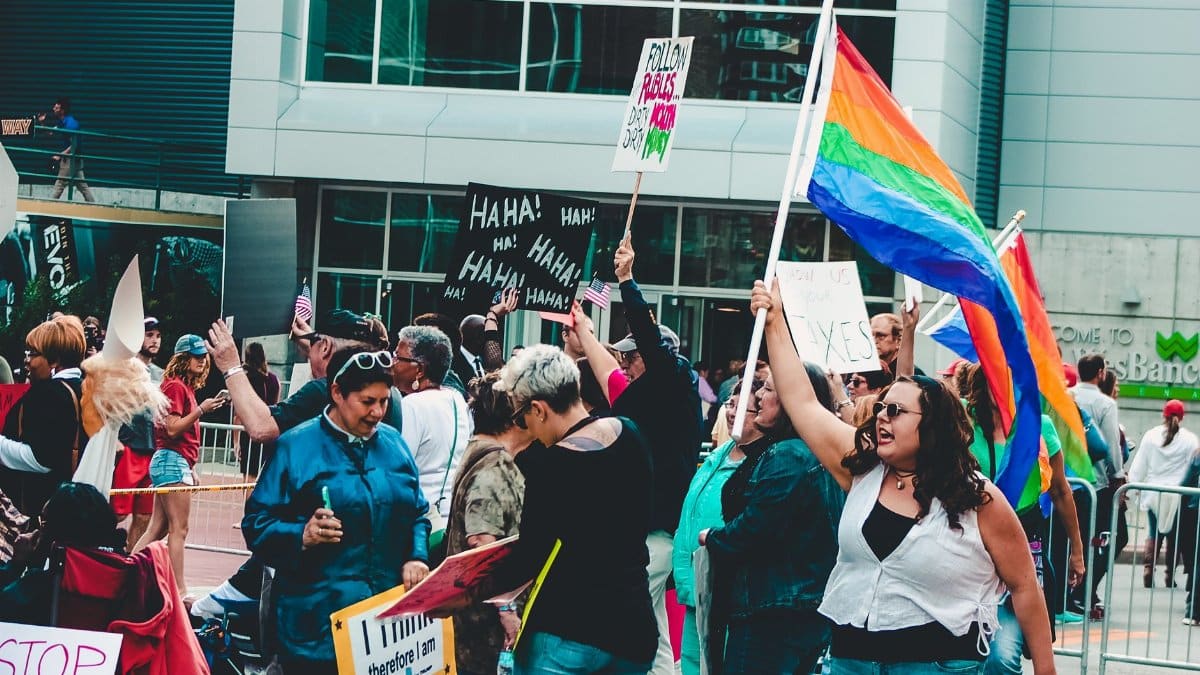 A lively LGBTQ pride rally with colorful flags, diverse people, and creative signs.