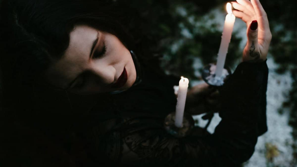 A woman in dark attire holds candles, creating a mystical and spiritual ambiance.