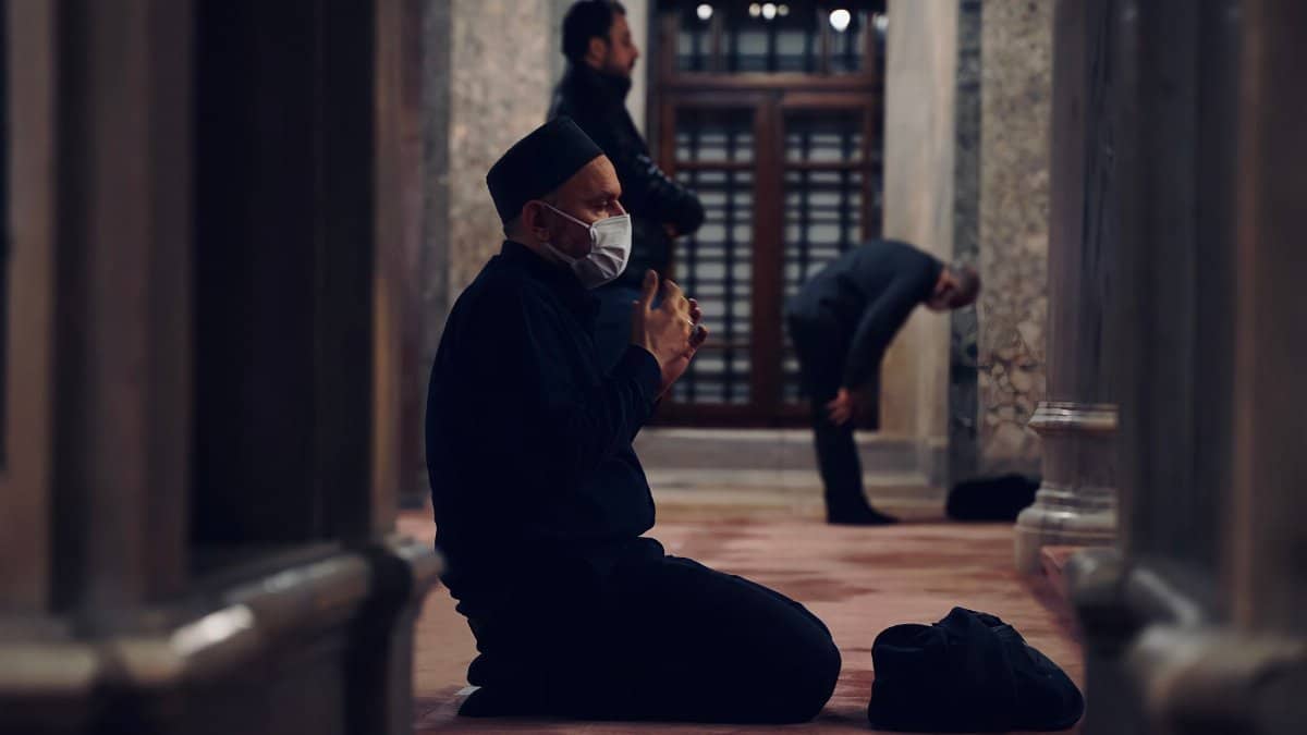 Man wearing a face mask and praying inside a mosque in Istanbul, reflecting on pandemic changes.