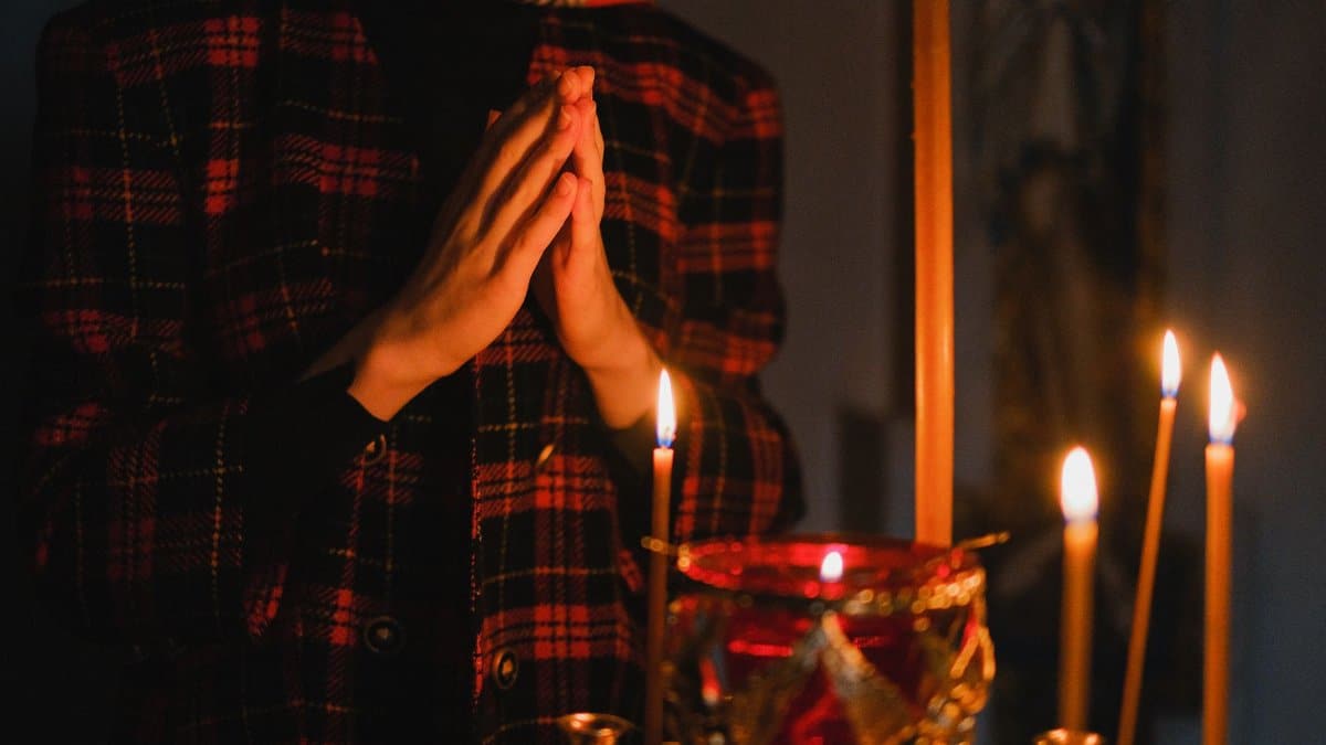 A person praying with candles in a dark, spiritual church setting.