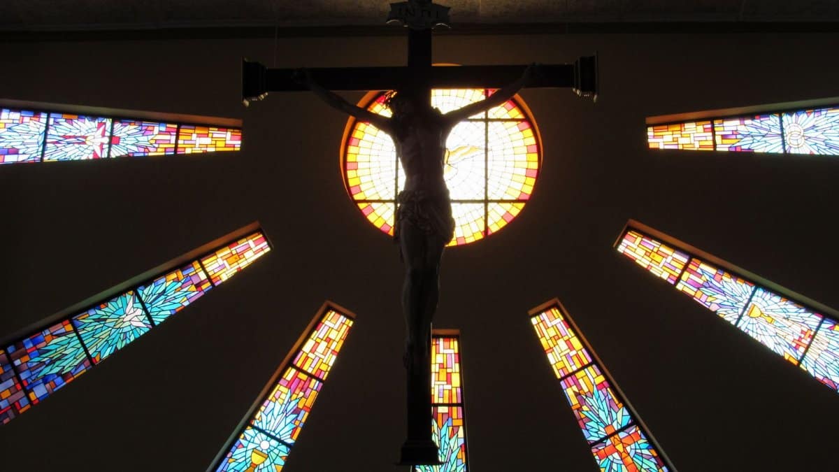 Silhouette of Jesus on the cross framed by vivid stained glass, evoking spiritual reflection.