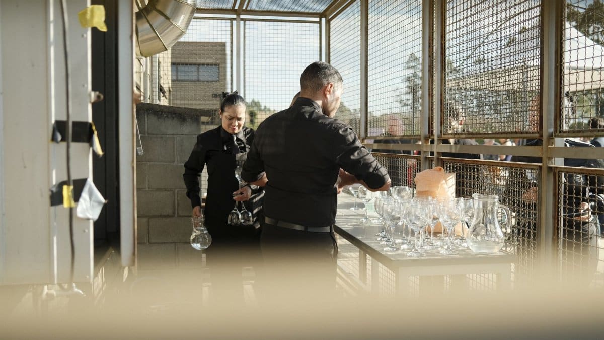 Catering staff setting up glassware for an outdoor event under the sun.