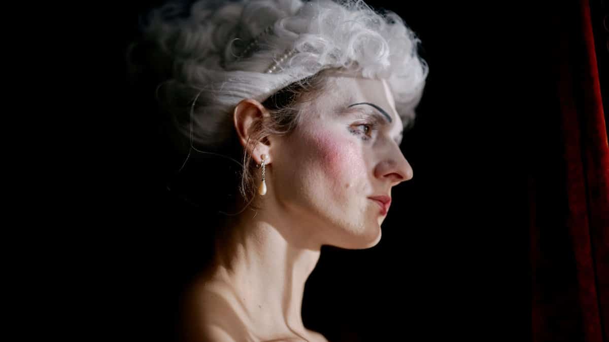 Artistic portrait of a woman in profile with classic makeup and wig, capturing theatrical essence.
